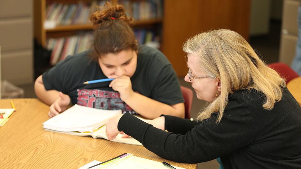 A female JCAE volunteer reviews material in a textbook with a female student